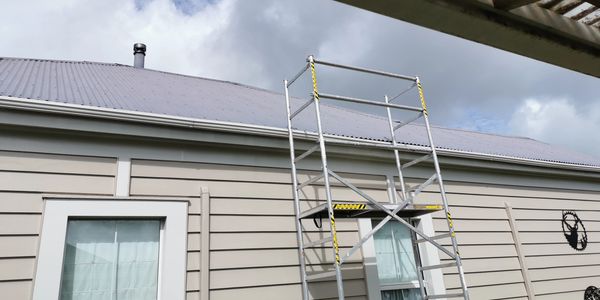 Scaffolding against a beige house with stormy sky.