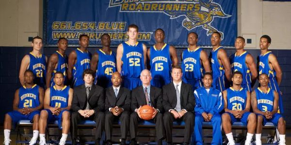 High school basketball team posing with coaches in a gymnasium.
