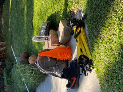 Sports training gear including shoes, cones, basketballs, and a water bottle on grass.