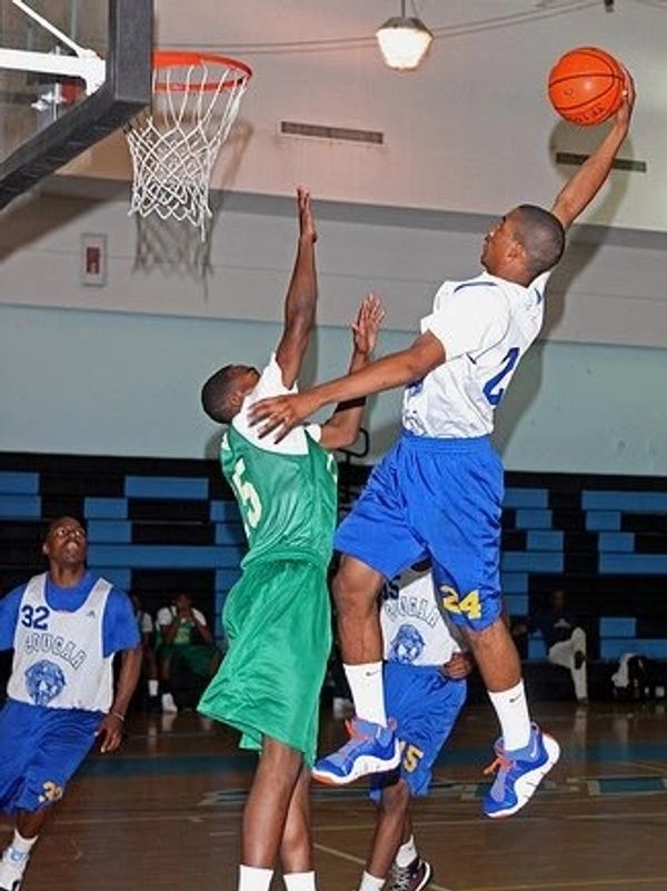 A basketball player in blue jumps to score over a defender in green.