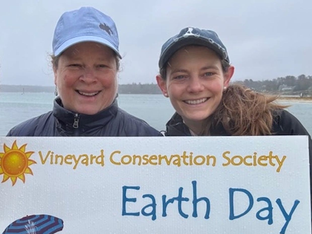 Two smiling women hold an Earth Day sign by the water.