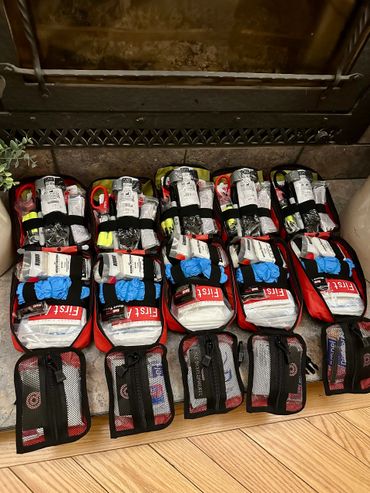 Five organized first aid kits laid out on a floor in front of a fireplace.