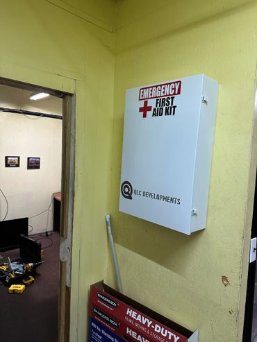 White emergency first aid kit mounted on a yellow wall in a cluttered room.