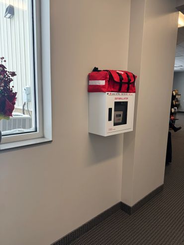 A defibrillator mounted on a beige wall with a red emergency bag on top.