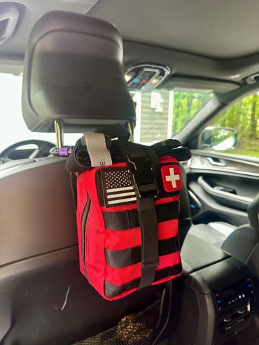 Red first aid kit attached to a car seat headrest with an American flag patch.