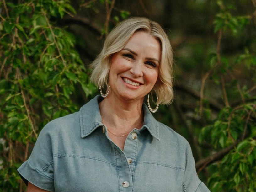 Smiling woman in denim shirt outdoors.