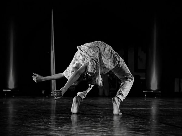 A dancer bends backward in a dramatic pose on stage, captured in black and white.