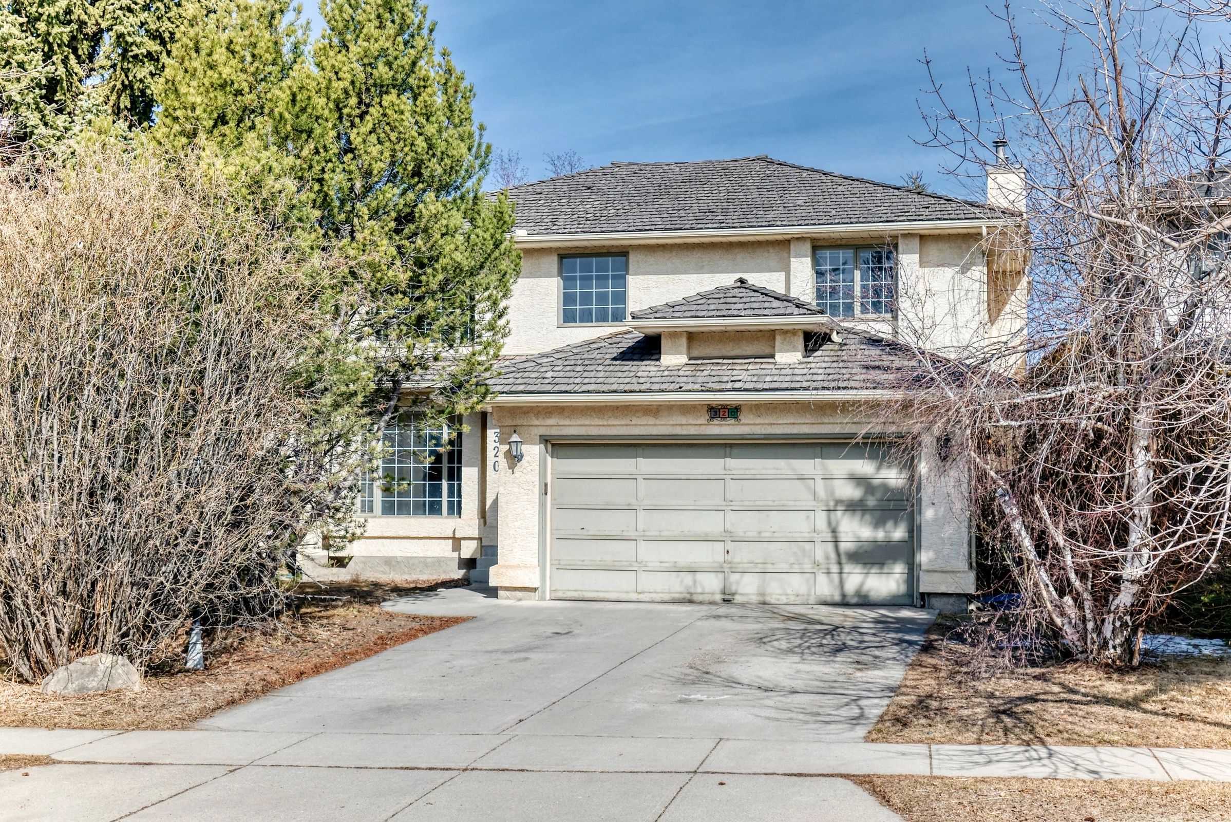 Two-story suburban house with a double garage and leafless trees in front.