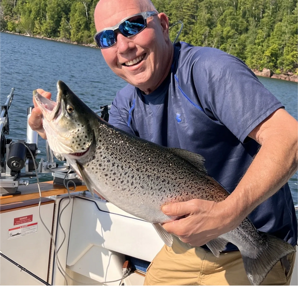 Smiling man holding a large fish on a boat under sunny skies.