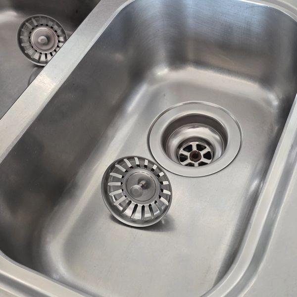 Close-up of a stainless steel kitchen sink with a detached drain strainer.