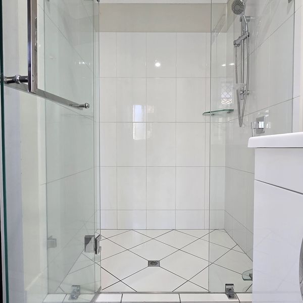 Modern glass shower enclosure with white tiled walls and floor.