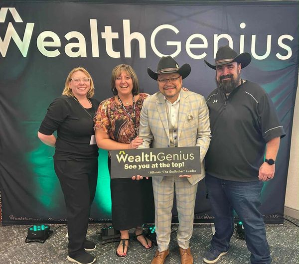 Four people smiling at a WealthGenius multi-family investor event holding a motivational sign.