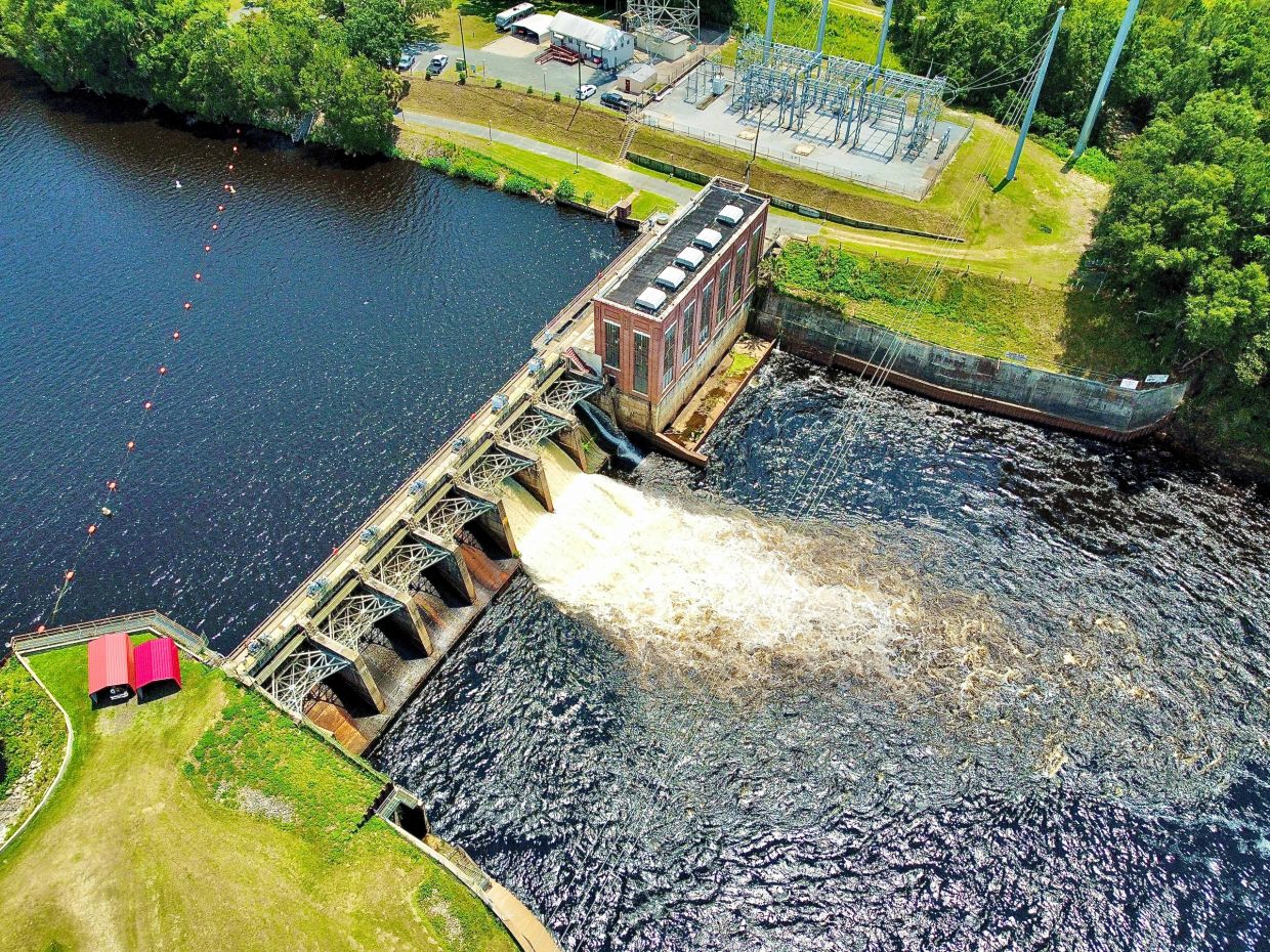 Aerial view of a dam releasing water with a power station nearby.