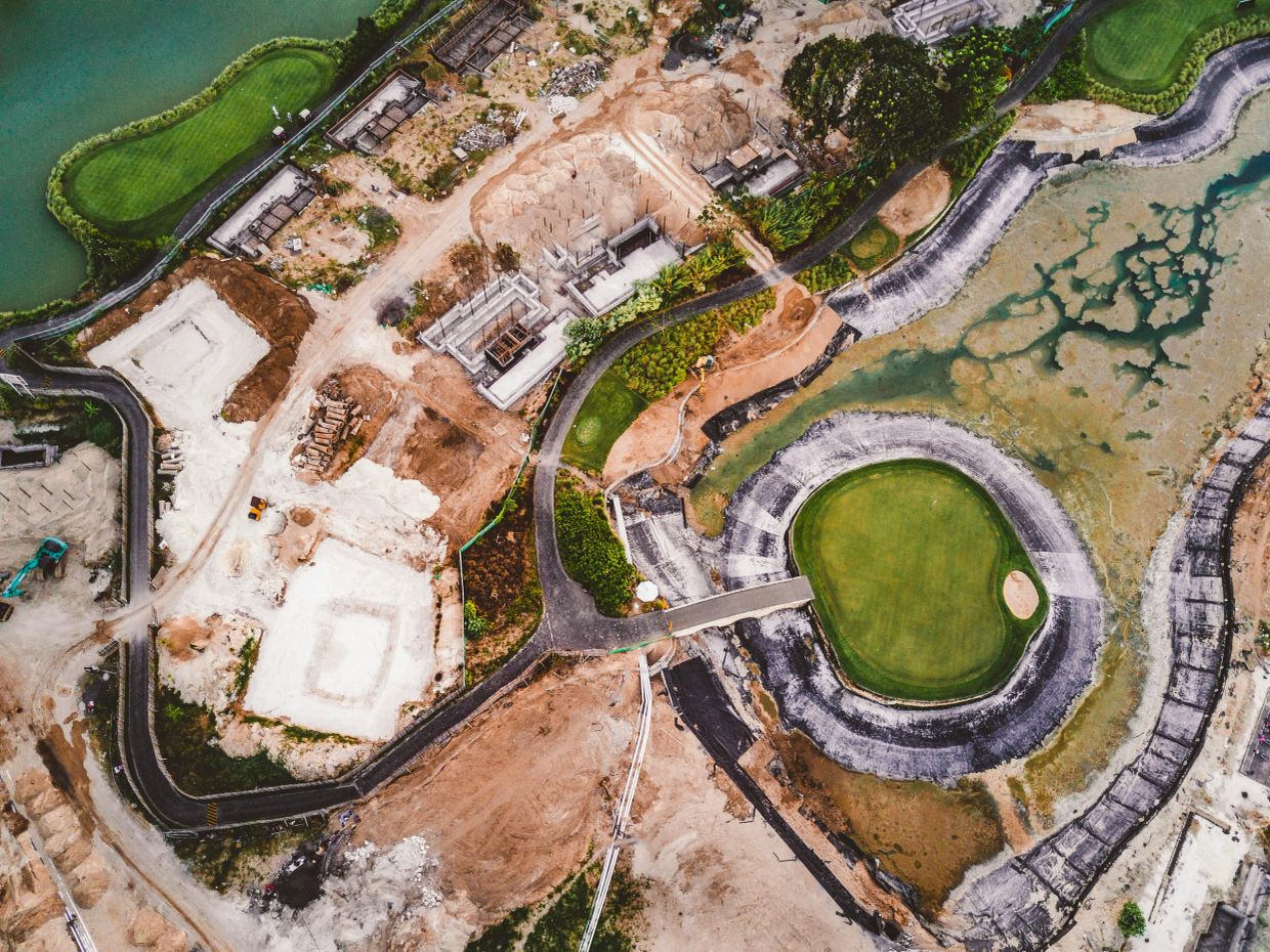 Aerial view of a partially constructed golf course with green patches and muddy areas.