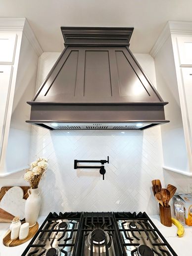 Modern kitchen stove with dark hood and white herringbone backsplash.