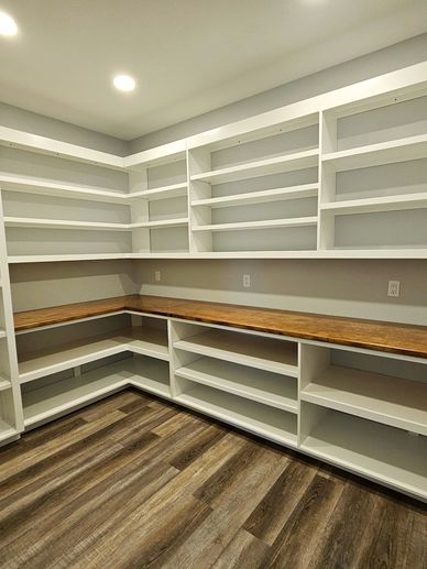Empty white shelving and wooden countertop in a modern pantry room.