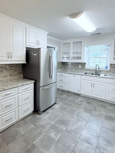 Bright modern kitchen with white cabinets and gray tiled floor.