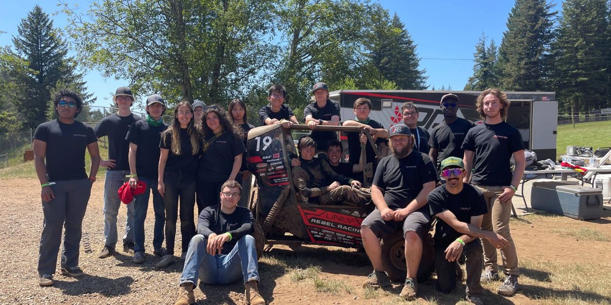 Group of people posing with an off-road vehicle outdoors.