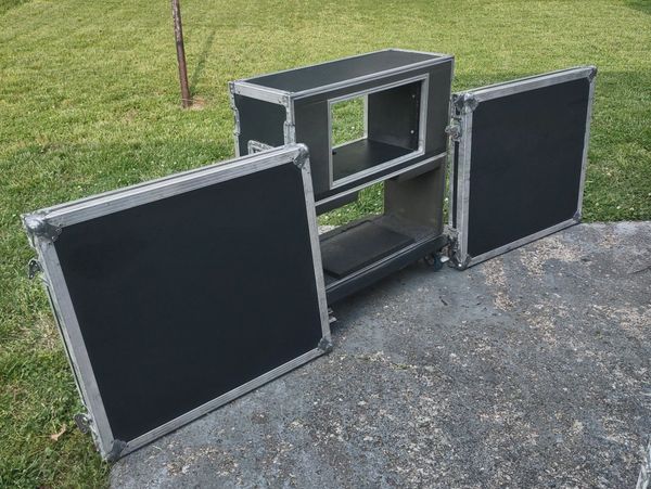Open black flight case with two detached doors on concrete and grass.