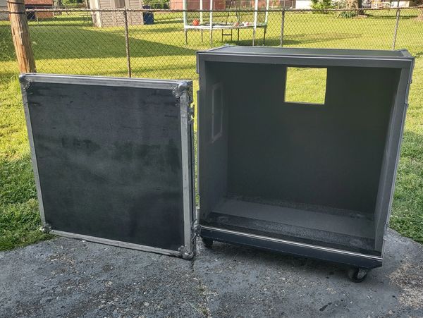 A large, open black equipment case with its lid detached, placed outdoors.