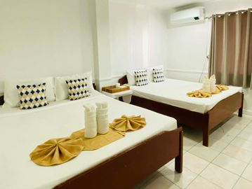 Bright hotel room with two neatly made beds and decorative pillows.