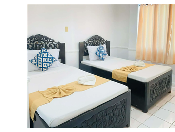 Two neatly made twin beds with decorative pillows and folded yellow runners in a bright room.