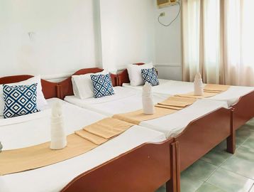 Three neatly made single beds with folded towels and patterned pillows in a bright room.
