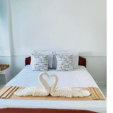 A neatly made bed with towel swans forming a heart shape.
