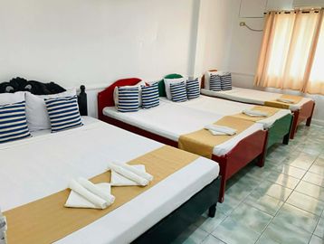 A row of neatly made beds with striped pillows and folded towels in a bright room.