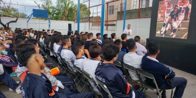 Students watch a sports game on a large outdoor screen.