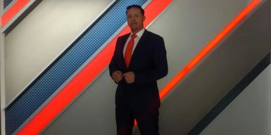 Man in a suit with red tie stands in front of a striped wall.