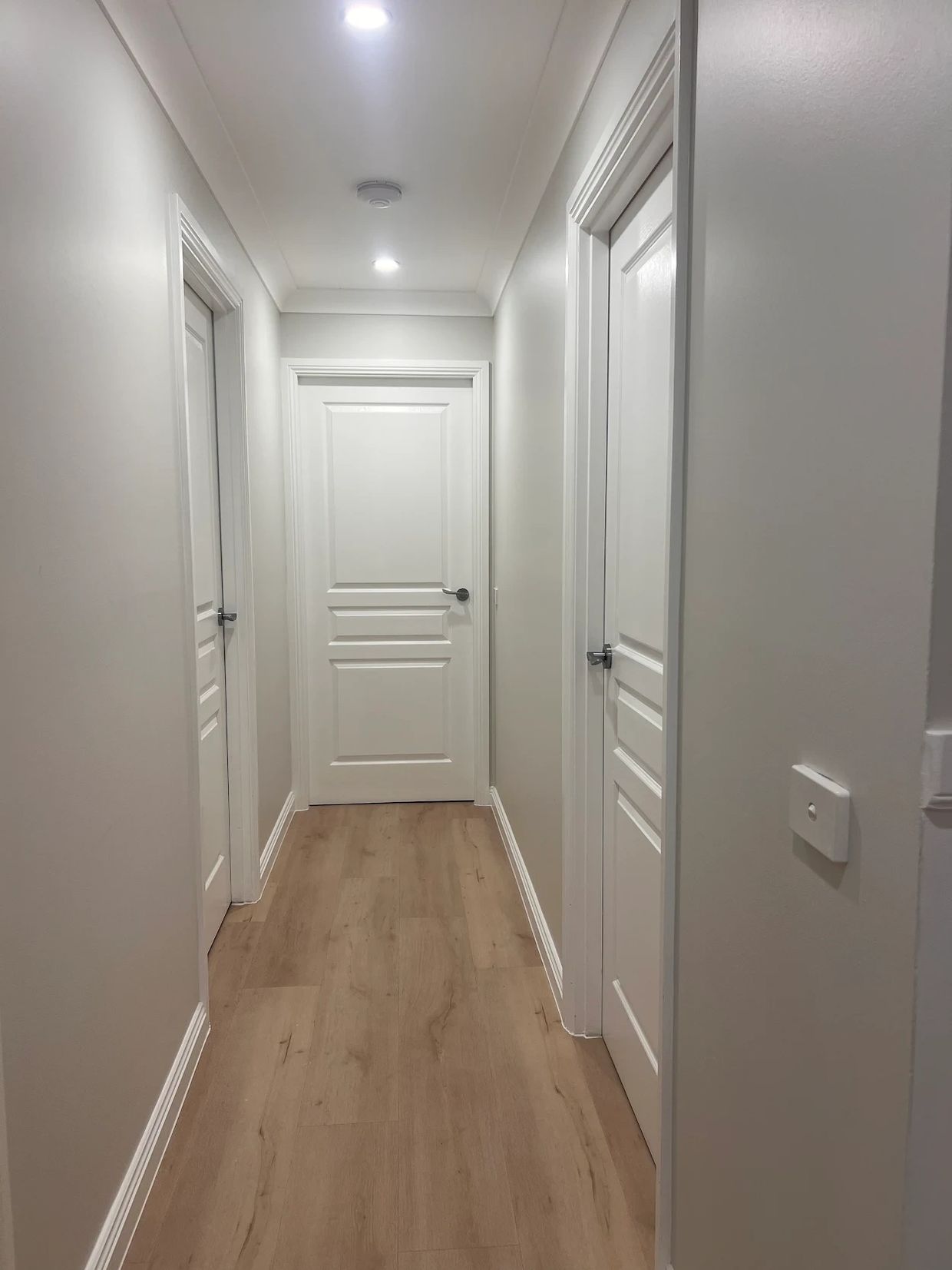 A clean, modern white hallway with wooden flooring and three closed doors.