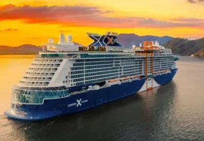 A Celebrity Cruises ship sailing at sunset near mountains.