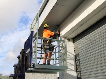 Worker in safety gear fixing camera on building from elevated platform.