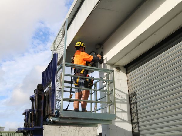 Worker in safety gear fixing camera on building from elevated platform.