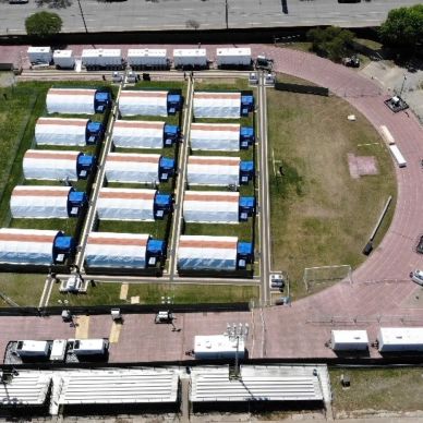 Aerial view of multiple rectangular structures with vehicles in a fenced area.