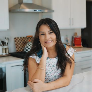 Smiling woman in a floral top leaning on a kitchen counter.