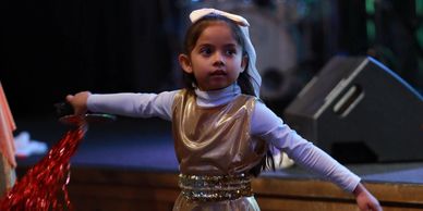 Young girl performing on stage with arms outstretched.