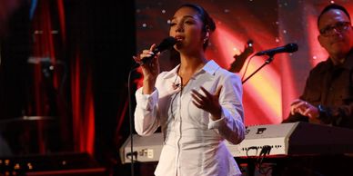 Woman singing passionately while holding a microphone on stage.