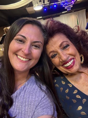 Two women smiling happily at a social event with colorful lighting.