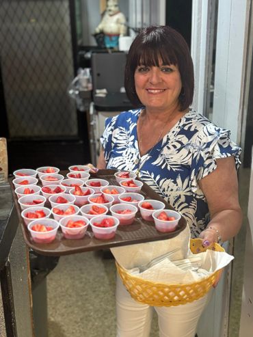 Woman smiling, holding tray of strawberry cups and basket of napkins.
