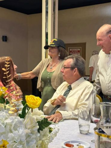 Group of people gathered around a table with flowers.