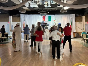 Couples dancing in a decorated hall with an Italian flag.