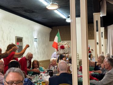 Group of elderly people dining in a restaurant with an Italian flag centerpiece.