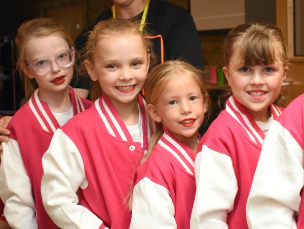 Five smiling girls in matching pink and white jackets posing together.