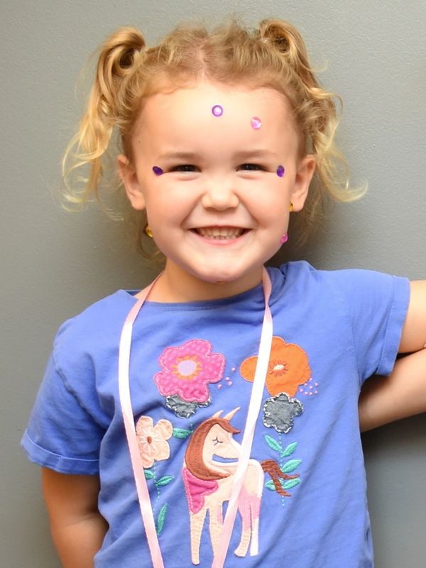 Smiling young girl with paint dots on her face and curly hair in pigtails.
