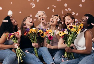 a group of women of all races sitting on the floor, holding flowers, flower petals falling