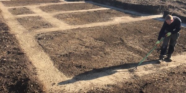Person preparing soil in a garden with divided plots on a sunny day.