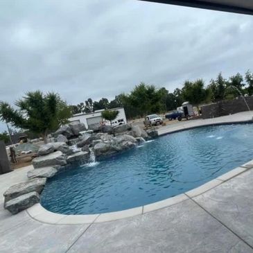 Outdoor pool with rock waterfall and cloudy sky.