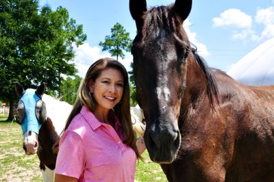 Woman smiling next to two horses outdoors.